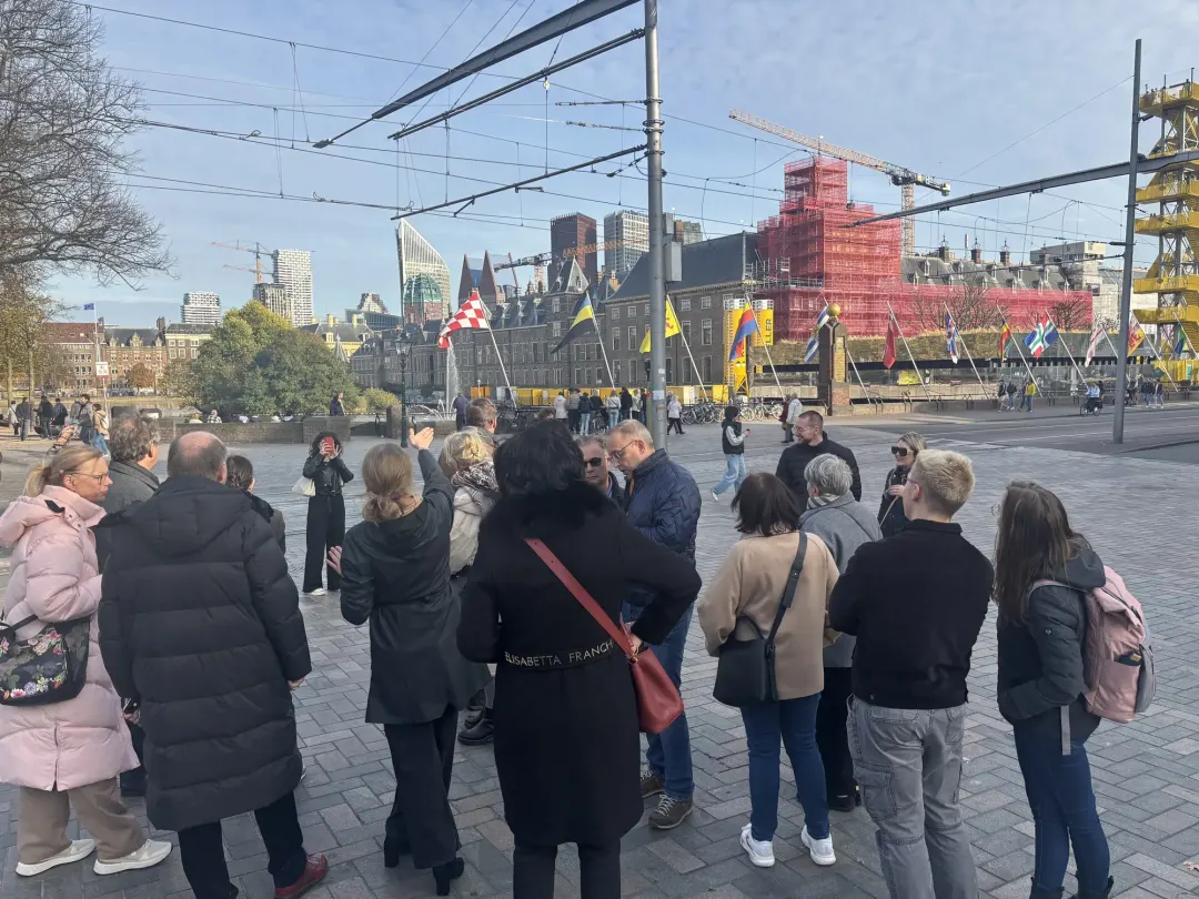 A tour group at the Hofvijver with international flags and the Binnenhof under renovation, The Hague