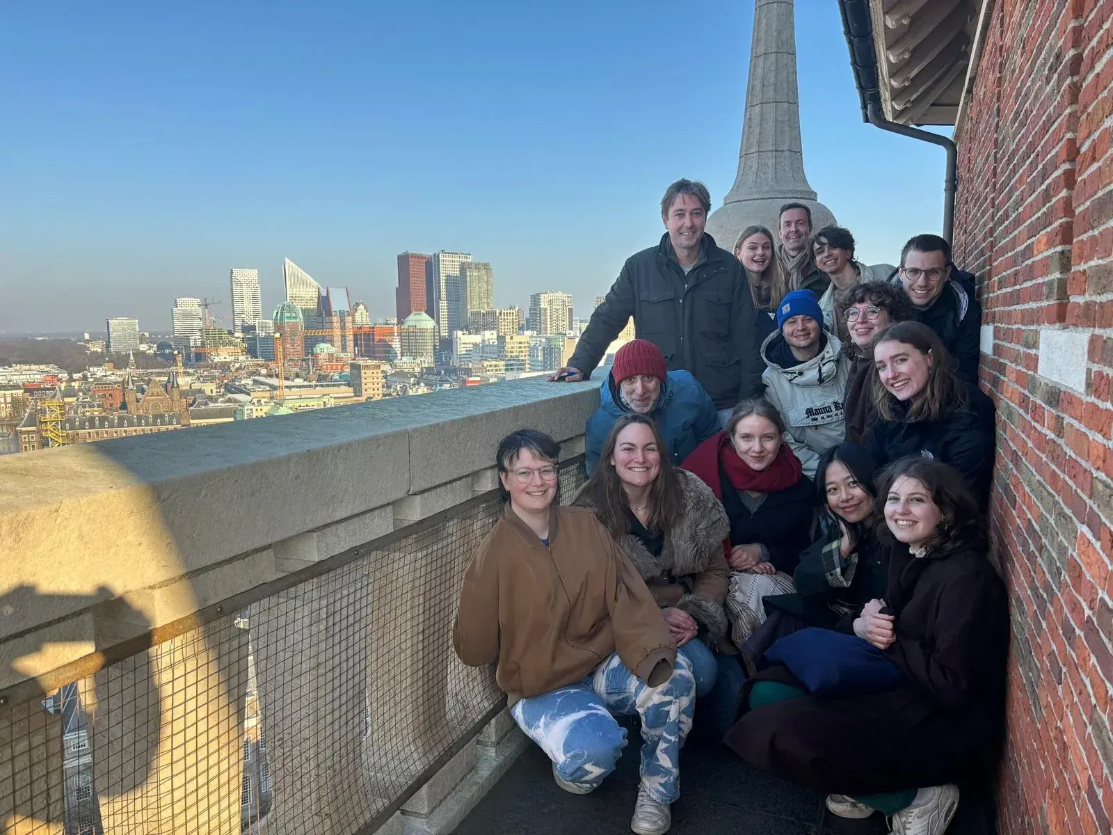 A smiling tour group at the top of the Grote Kerk tower, with The Hague skyline behind them
